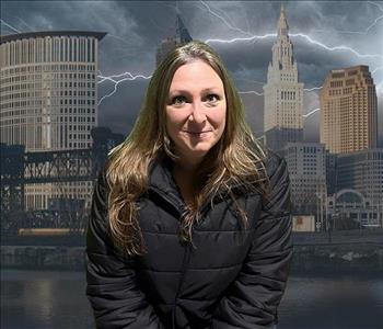 Picture of a blonde woman in a black winter coat in front of a stormy Cleveland background